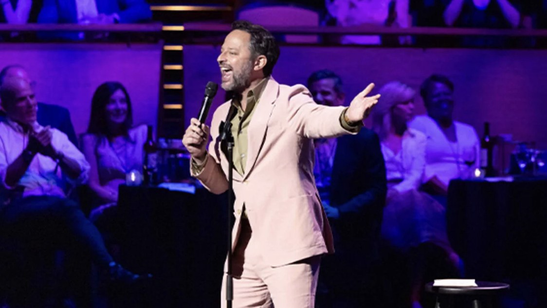 A comedian with a microphone performing for a seated audience at a Comedy vs Cancer event